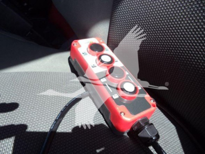 Remote control with red body and black circular buttons resting on a car seat. Cable attached.