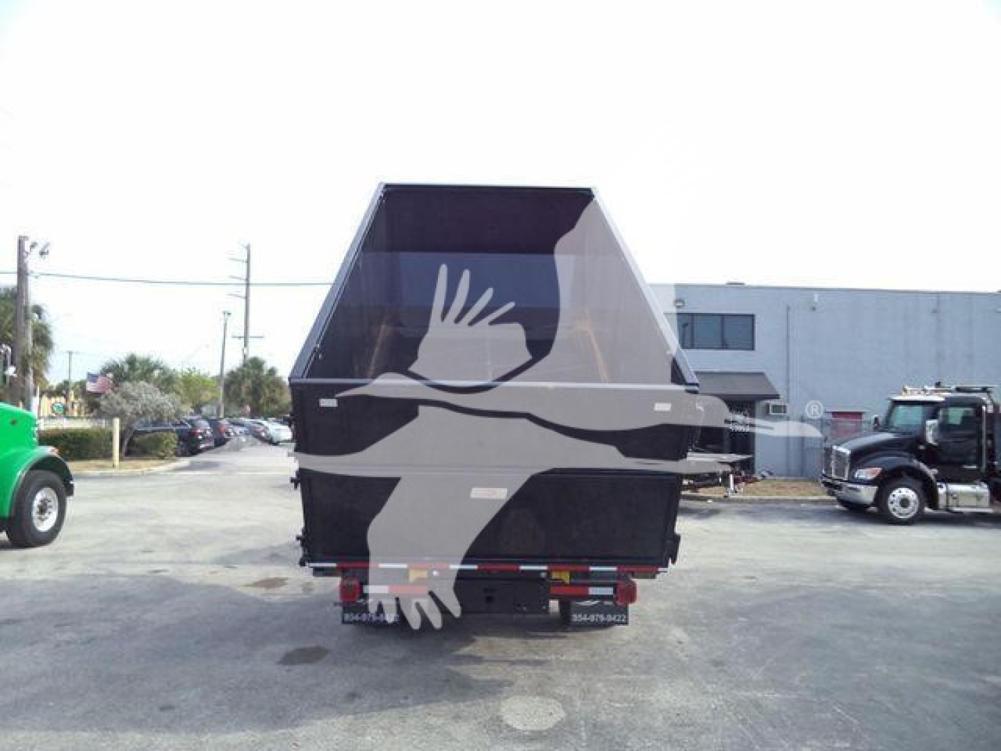 Back of a 2023 Chevrolet Silverado 6500HD roll-off truck with a large black dump bed and gray graphic of a hand. License plate area not legible.