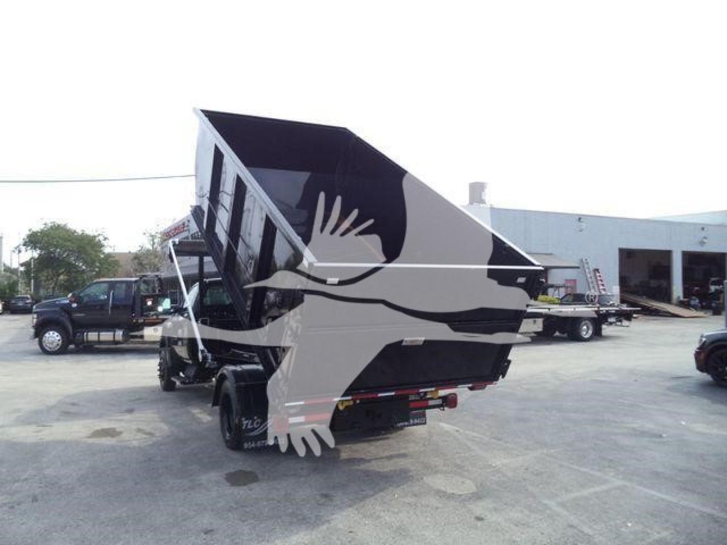 Dump truck bed raised on a Chevrolet Silverado 6500HD roll-off, with black dump body and blue sky