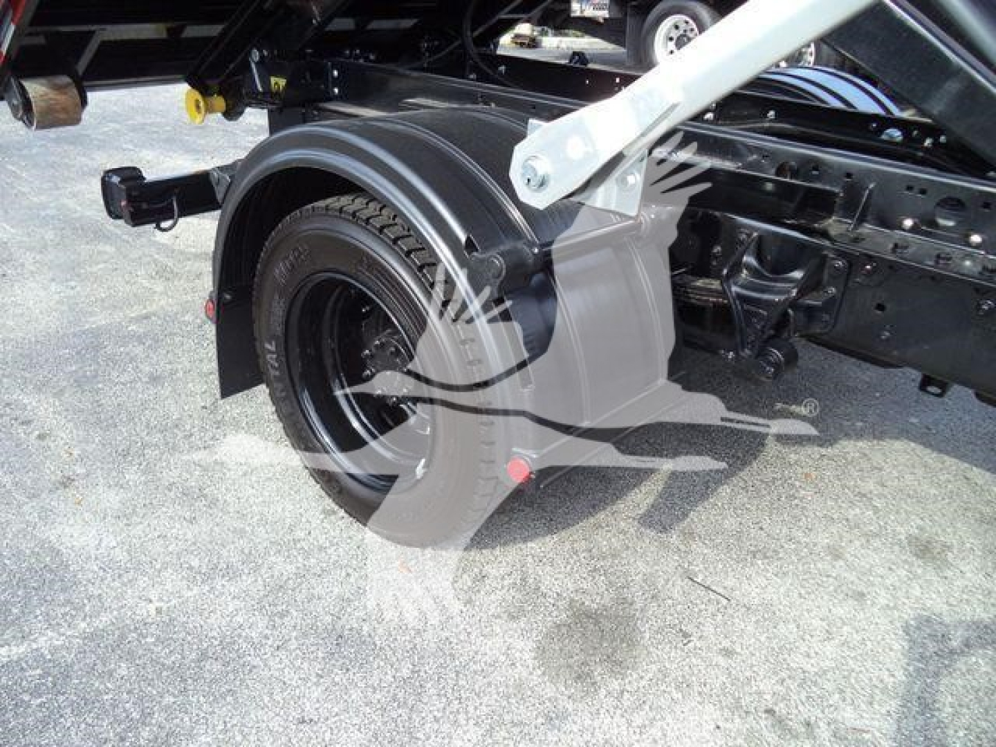 Truck chassis and rear wheel area of a 2023 Chevrolet Silverado 6500HD rolloff dump truck showing wheel, fender, and frame components.
