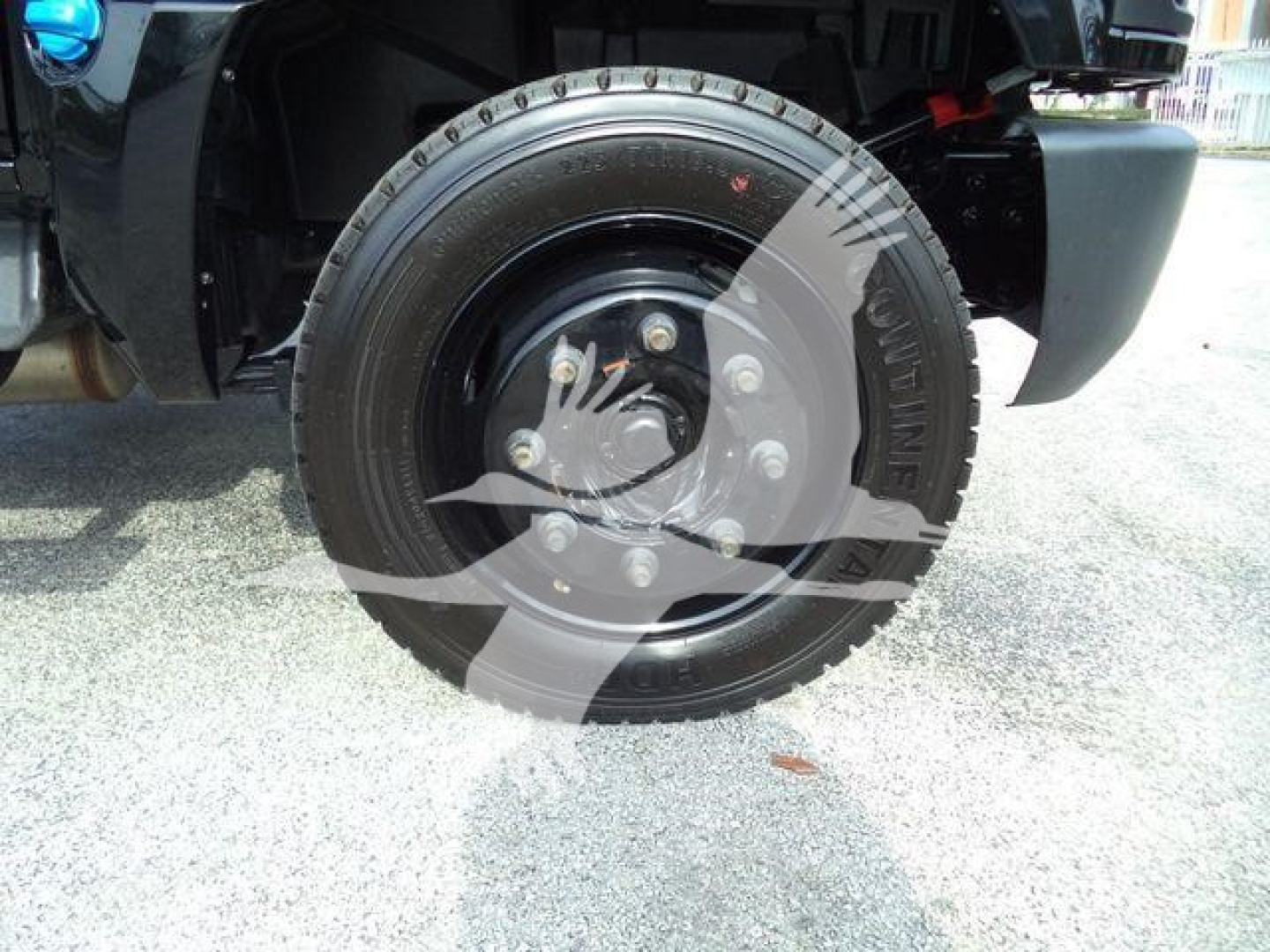 Wheel and tire on front of 2023 Chevrolet Silverado 6500HD dump truck showing steel wheel, lug nuts, and tire with tread, fender and part of suspension visible.