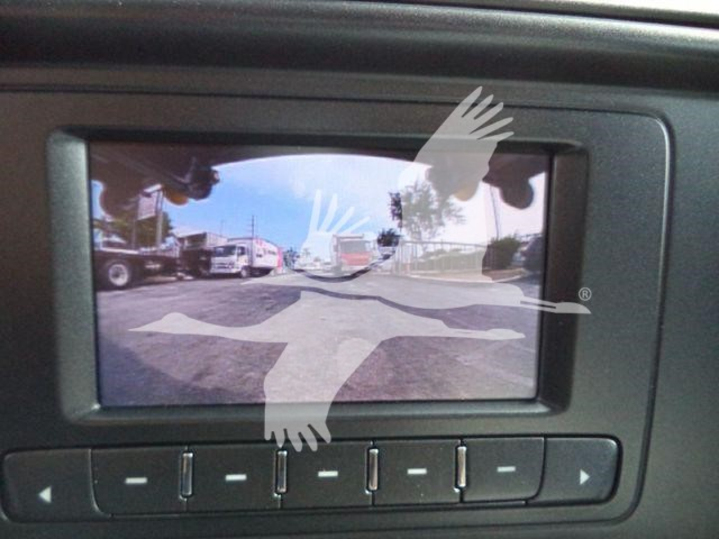 Back-up camera view showing a parking lot with trucks; in-view on-screen display with control buttons below.