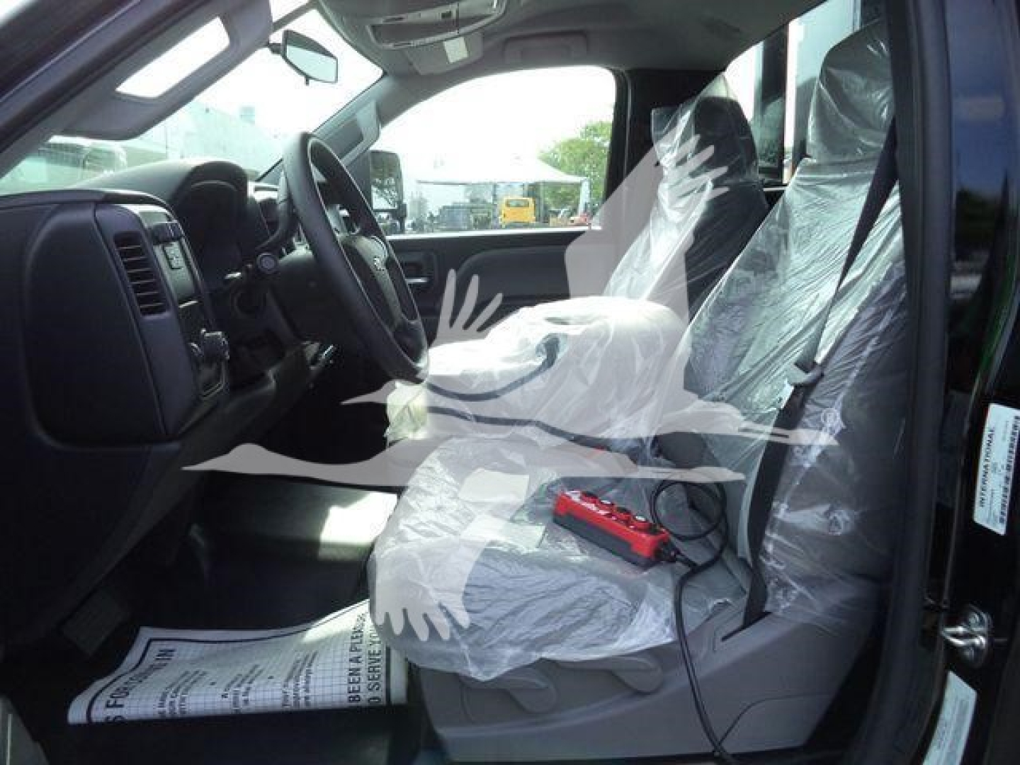 Truck interior showing front seats wrapped in protective plastic, steering wheel, dashboard, and gear shifter in a Chevrolet Silverado cab.