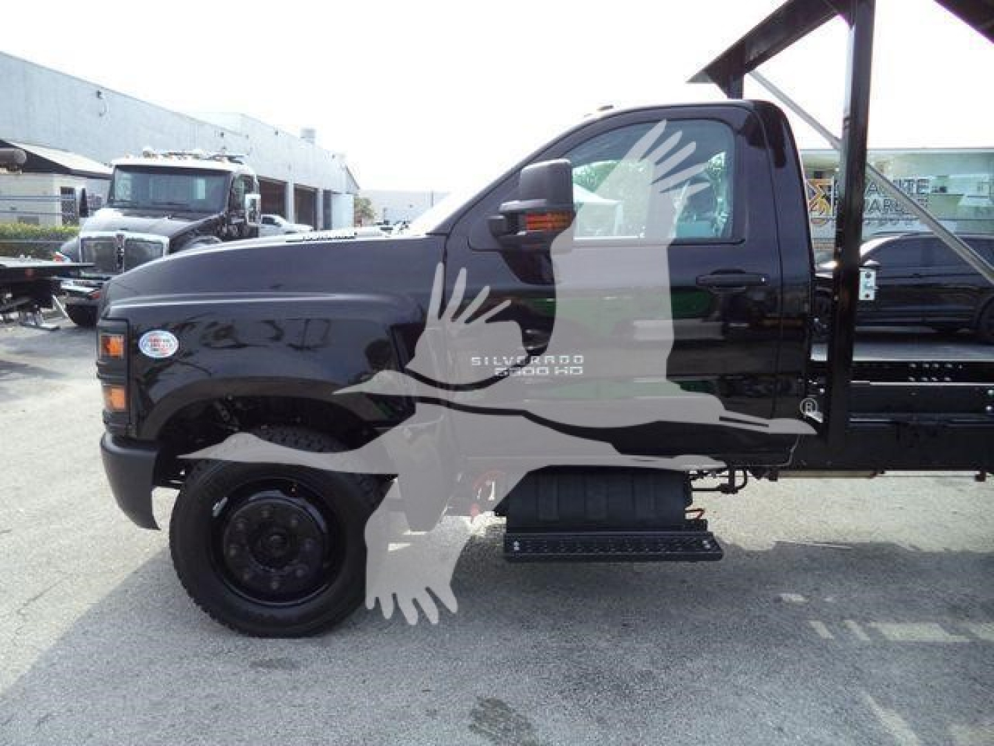 Chevrolet Silverado 6500HD flatbed with dual rear wheels and extended cab, side view showing step rail and hydraulic rollover setup.