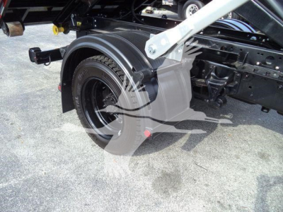 Truck chassis and rear wheel area of a 2023 Chevrolet Silverado 6500HD rolloff dump truck showing wheel, fender, and frame components.