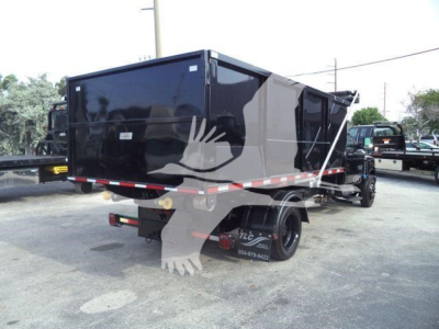 Truck bed showing black dump body with reflective tape and dual rear wheels in a dealership lot.