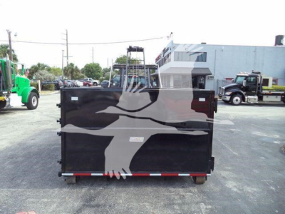 Truck dump body with a black side panel featuring a white bird graphic and rear view showing tailgate with reflective stripe; background shows a dealership lot with other trucks.