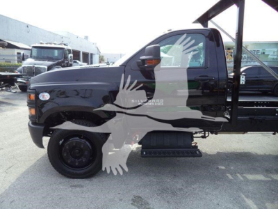 Chevrolet Silverado 6500HD flatbed with dual rear wheels and extended cab, side view showing step rail and hydraulic rollover setup.