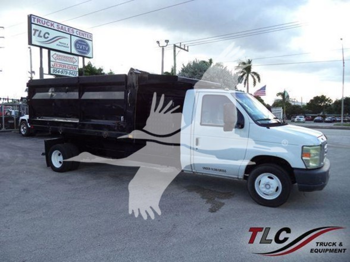 Ford E-450 dump truck with black dump bed and white cab. Visible text includes TLC Truck Sales Center sign and logo in lot; no legible VIN or specs on image portion.
