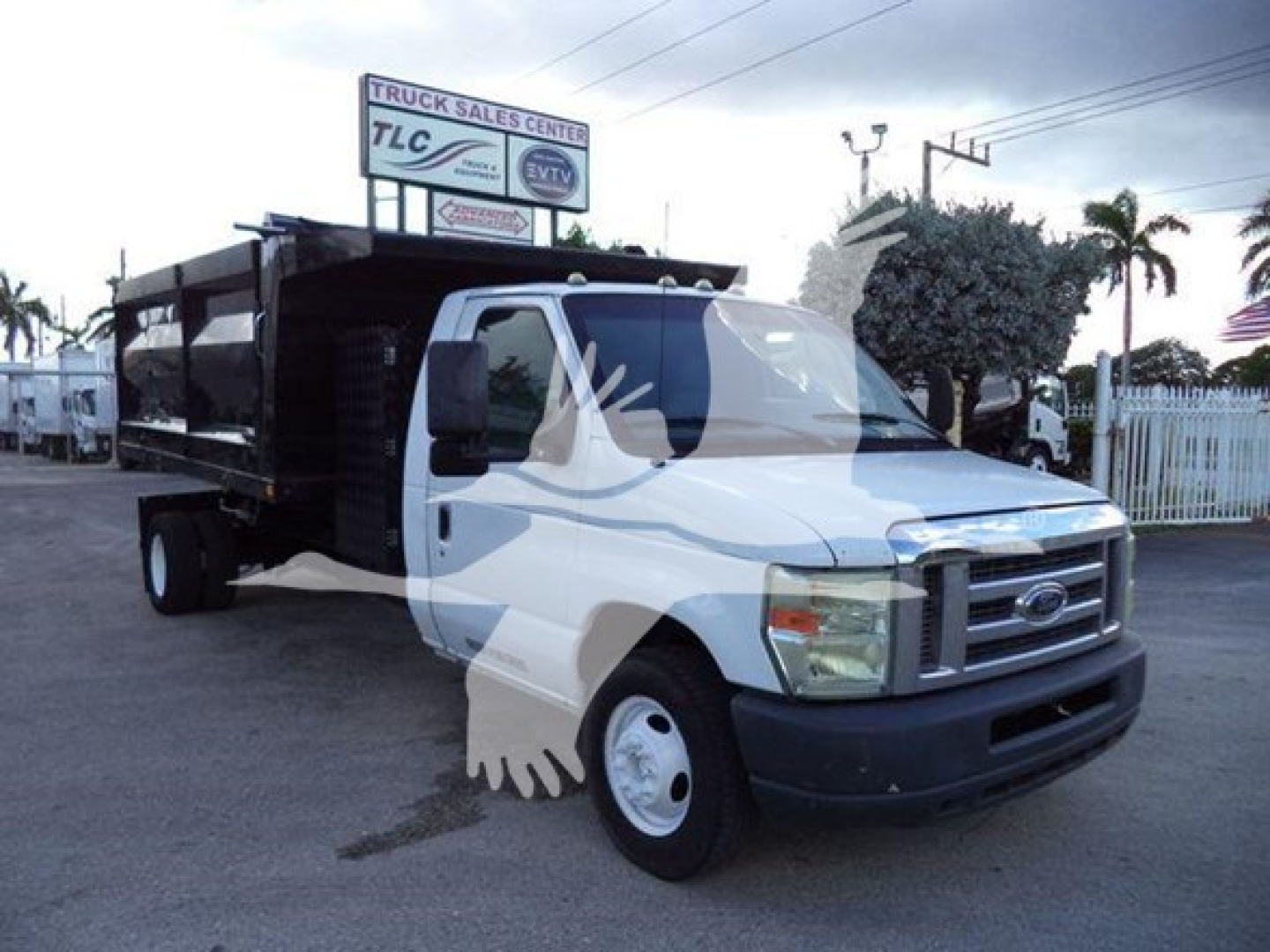 Ford E-450 dump truck in a lot with front-right view and lettering on sign in background.