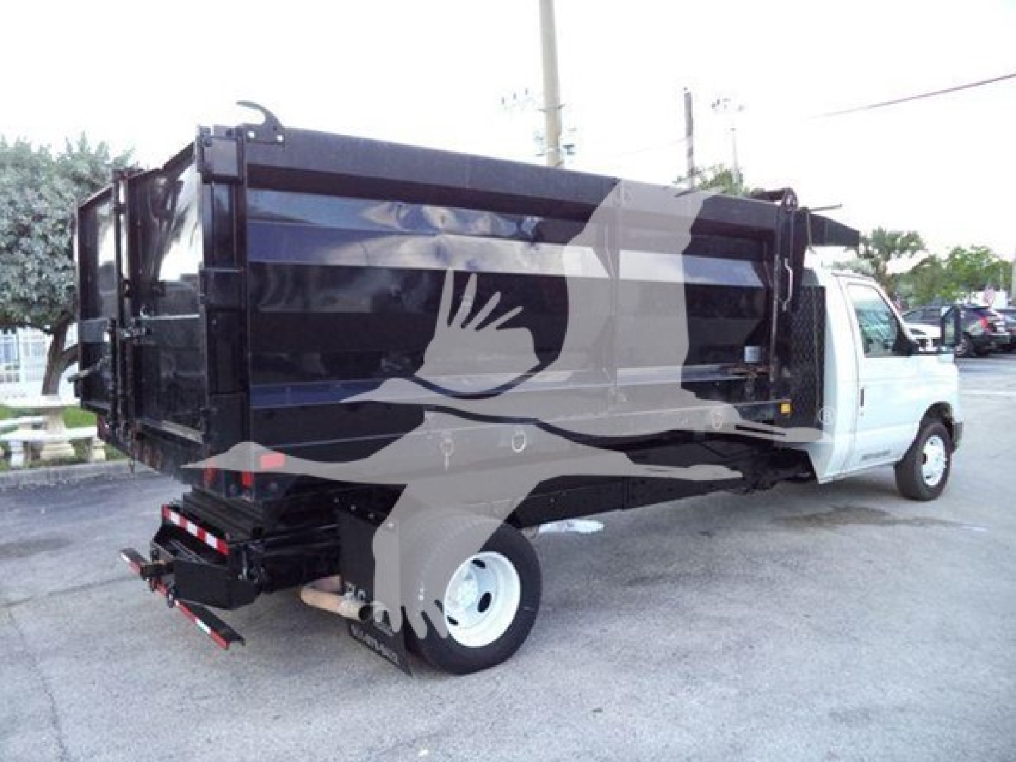 Dump truck with black dump bed and white cab, side view showing rear hydraulic dump mechanism and wheel. No visible text legible.
