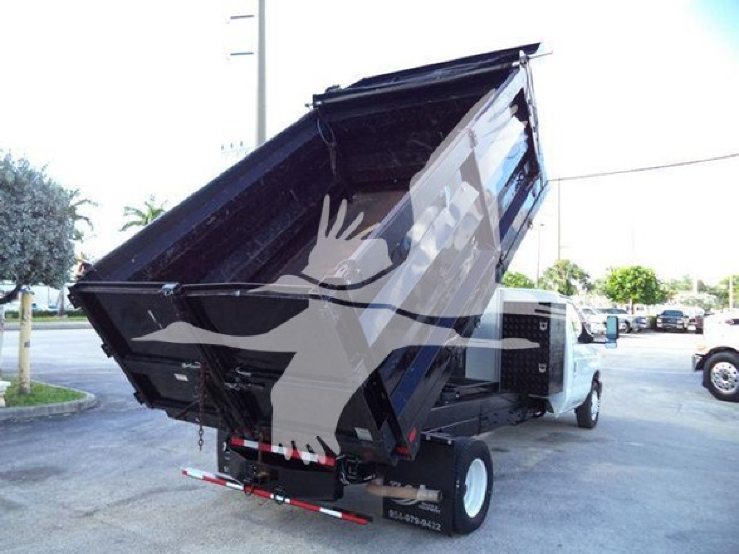 Dump truck bed and cab of a 2011 Ford E450 with a raised black dump body, white truck, visible hydraulic mechanism and rear lights.