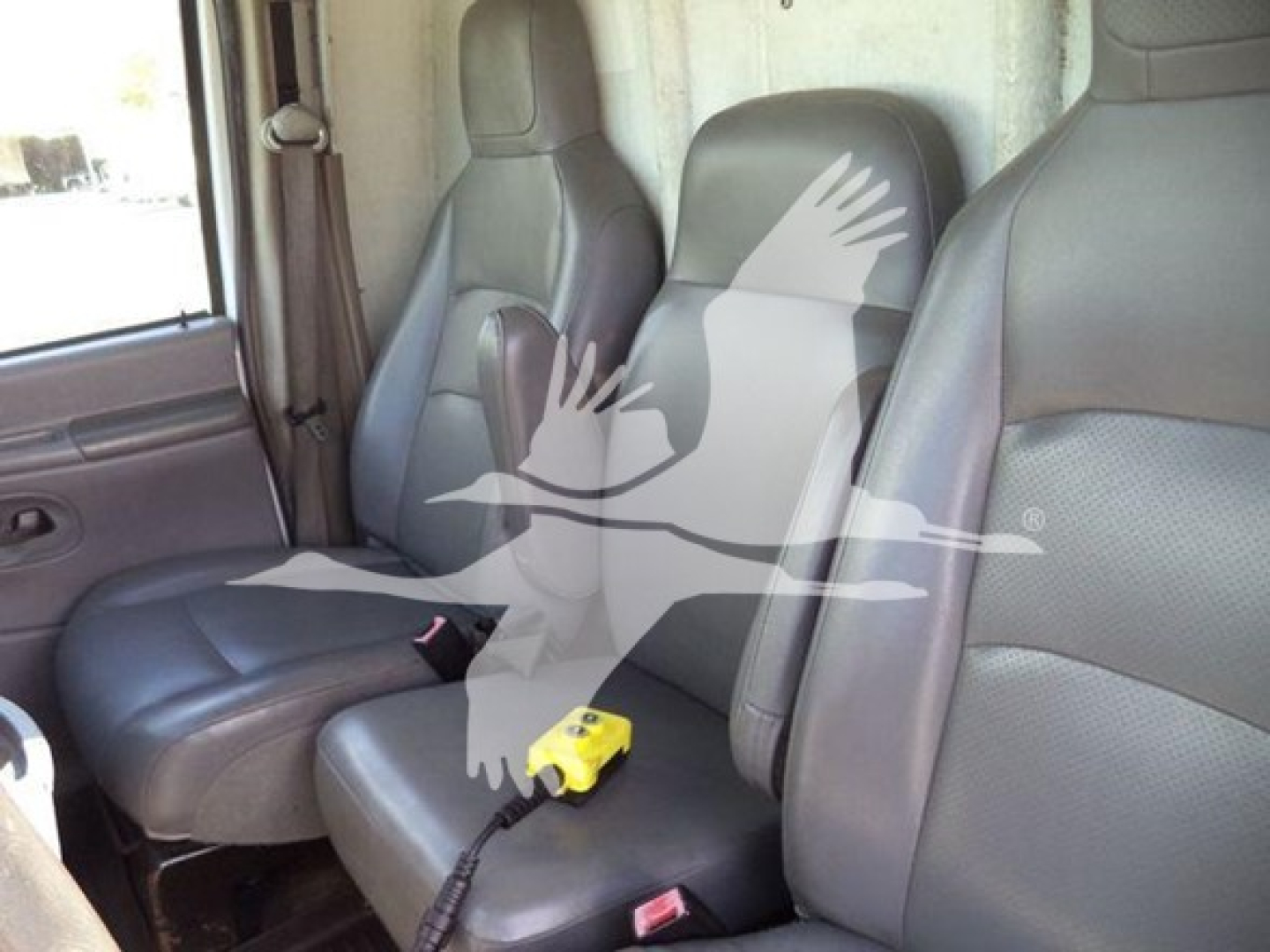 Ford E-Series van interior front seats with a yellow portable device on the center console; watermark of a bird graphic overlaying the image.