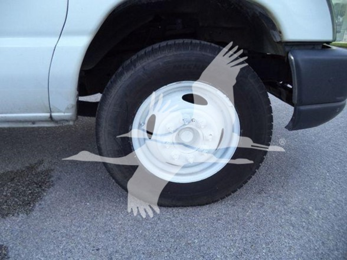 Ford E450 wheel and tire visible in front fender area; steel wheel rim with hubcap; part of front bumper and wheel well edge visible.