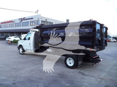 Ford E450 dump truck with a black dump body, white cab, and front side view; no visible text on the vehicle besides stock signage in background building.