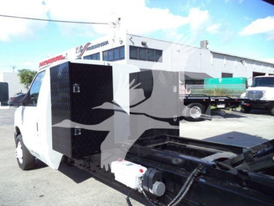 Dump truck body on a Ford E-450 chassis with a black diamond-plate tool/storage compartment open on the side.