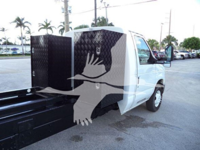 Ford E-Series van side view showing a diamond-plate metal toolbox mounted behind the cab on a white truck, with a flatbed/material handling surface.
