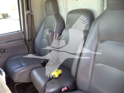 Ford E-Series van interior front seats with a yellow portable device on the center console; watermark of a bird graphic overlaying the image.