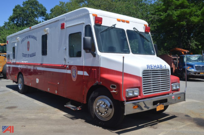 Emergency vehicle: 1990 Chevrolet P60 forward-control chassis ambulance with red and white livery, REHAB-1 marking, large grille, side access doors, and emergency lighting.