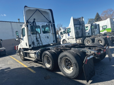 Truck chassis and cab of a 2021 Freightliner Cascadia 116 daycab showing rear triple-axle configuration and raised cab with visible VIN plate area.