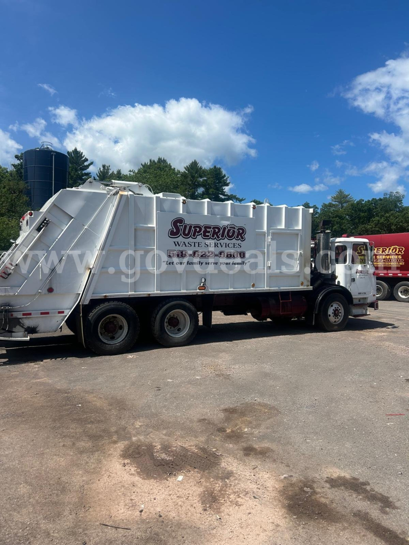 Autocar XPeditor garbage truck in service with a Superior Waste & Services banner on the side; side view showing rear compactor and truck wheels.