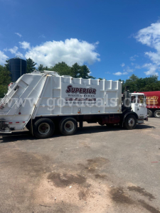 Autocar XPeditor garbage truck in service with a Superior Waste & Services banner on the side; side view showing rear compactor and truck wheels.