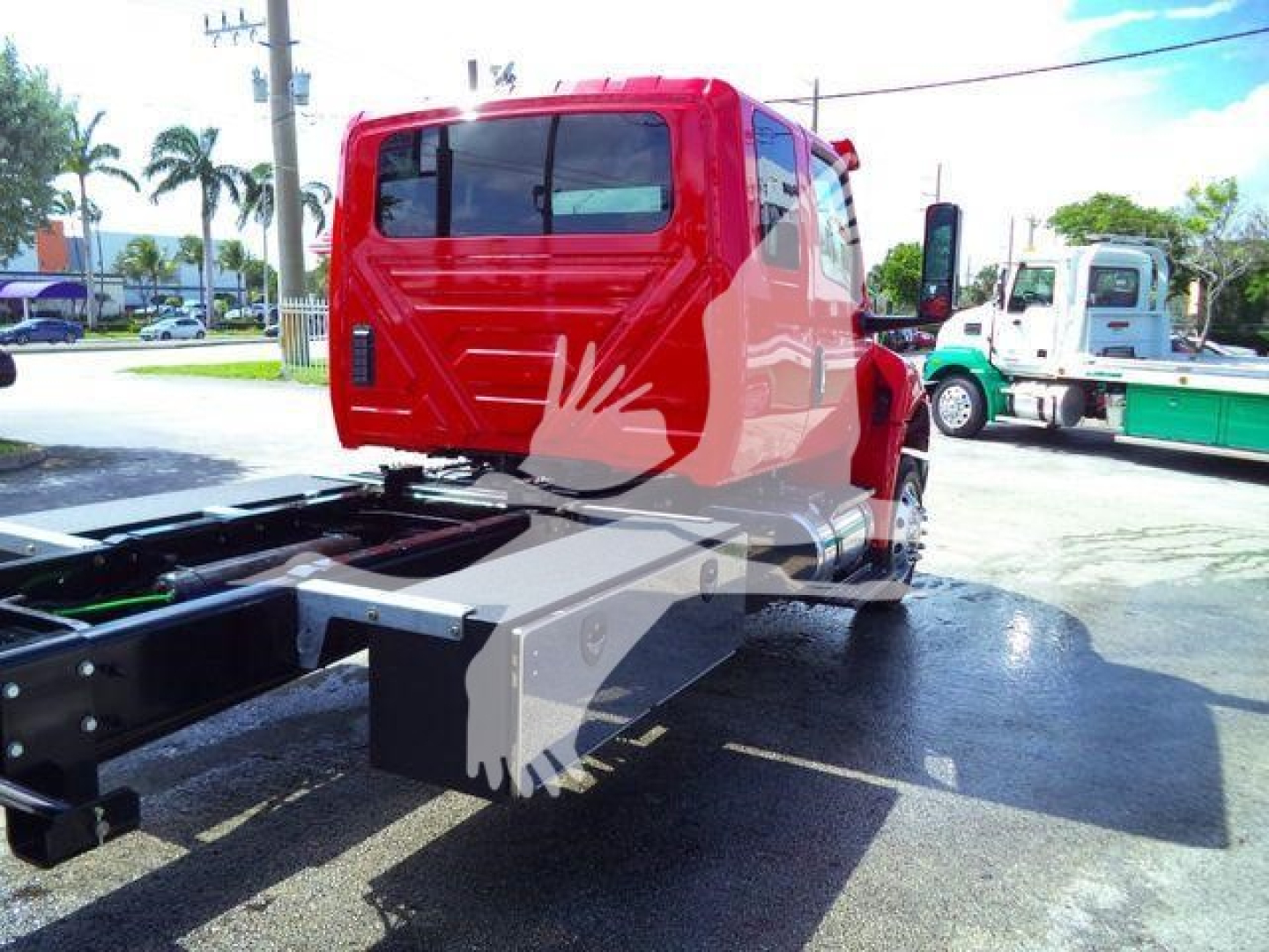 Red International MV cab with rollback chassis visible from rear/side; no visible model numbers or serials on cab; other trucks in background.