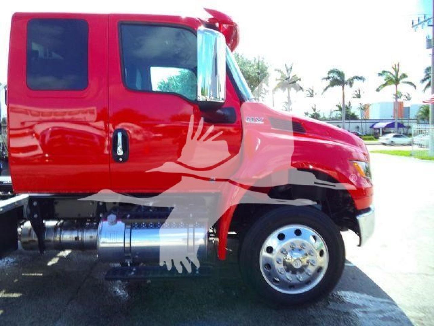 Truck side view showing red 2027 International MV rollback truck cab and front wheel with chrome fuel tank and emblem visible.