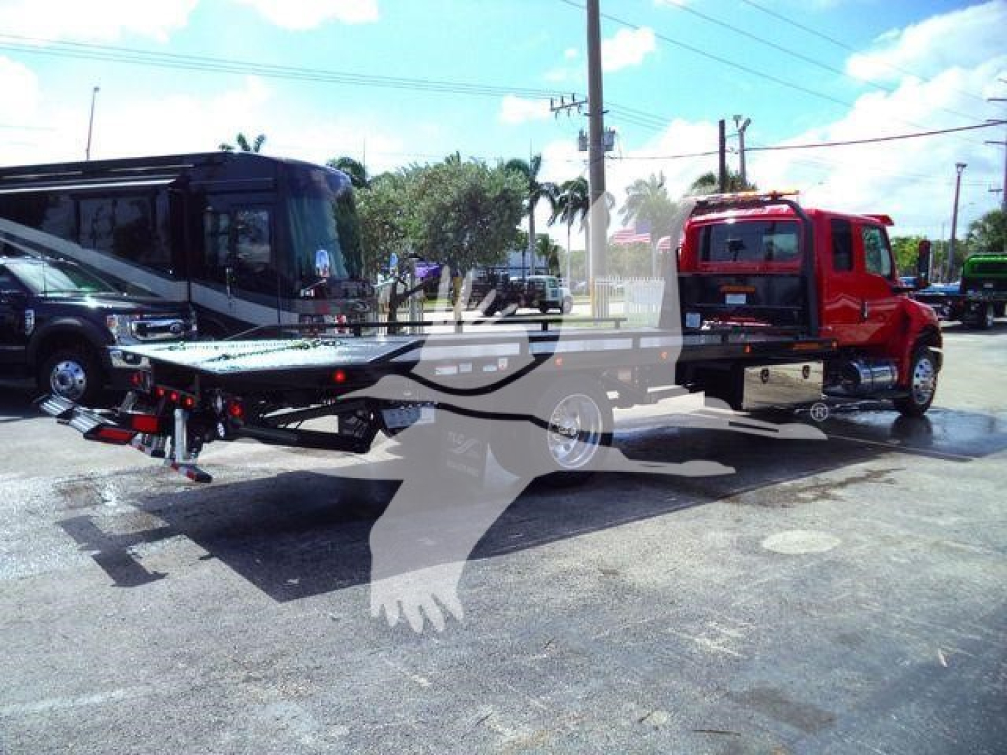 Truck with rollback tow bed attached, red cab on right, black trailer on left, showroom lot in background.