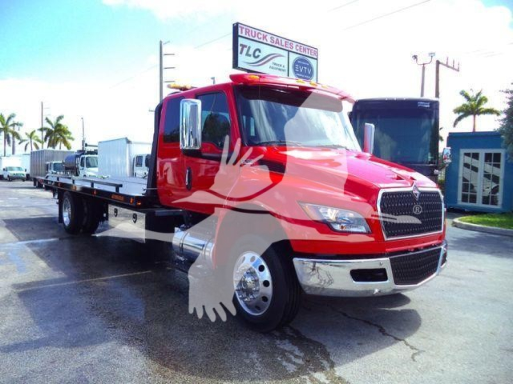 International MV tow truck in red, front view with flatbed, dealership sign on roof, tropical background.