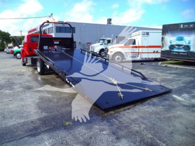 Truck flatbed tow truck in a lot with other trucks and mobile units visible.