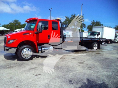 Red 2027 International MV rollback truck with a flatbed and side mirrors visible in a dealership lot.
