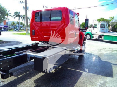 Red International MV cab with rollback chassis visible from rear/side; no visible model numbers or serials on cab; other trucks in background.