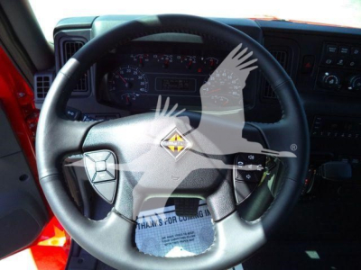 Truck interior steering wheel and dashboard from a 2027 International MV rollback truck; visible steering wheel center badge and instrument cluster.