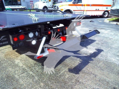 Flatbed tow truck with a hydraulic rollback and steps, rear view showing lights and metal platform; sticker text partially visible on left side and rear bumper