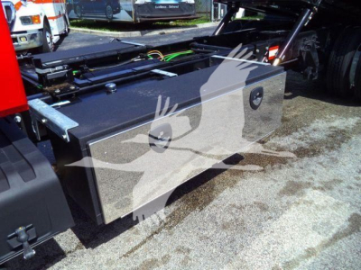 Fuel tank/storage box mounted on truck chassis with metallic silver finish and access panels, connected to cab-frame plumbing and wiring, on a rollback truck.