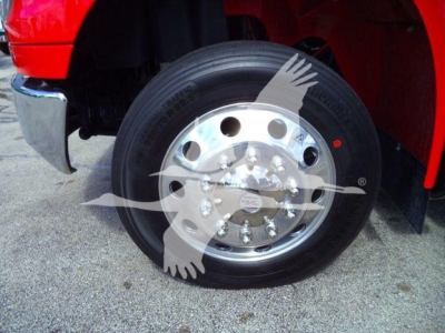 Truck wheel and tire with chrome hubcap on front of red International MV rollback truck, partial fender and chrome bumper visible.