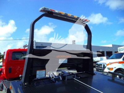 Truck equipment image showing a foldable rollback lever system with a clear windshield and a black frame; red cab in background; brand name Jerr-Dan visible on the frame; blue sky.