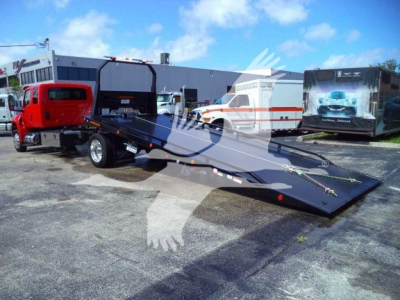 Industrial rollback tow truck with a long flatbed trailer in a dealership lot. Visible text includes MV607RED stock number and vehicle category: Rollback, Trucks, New.