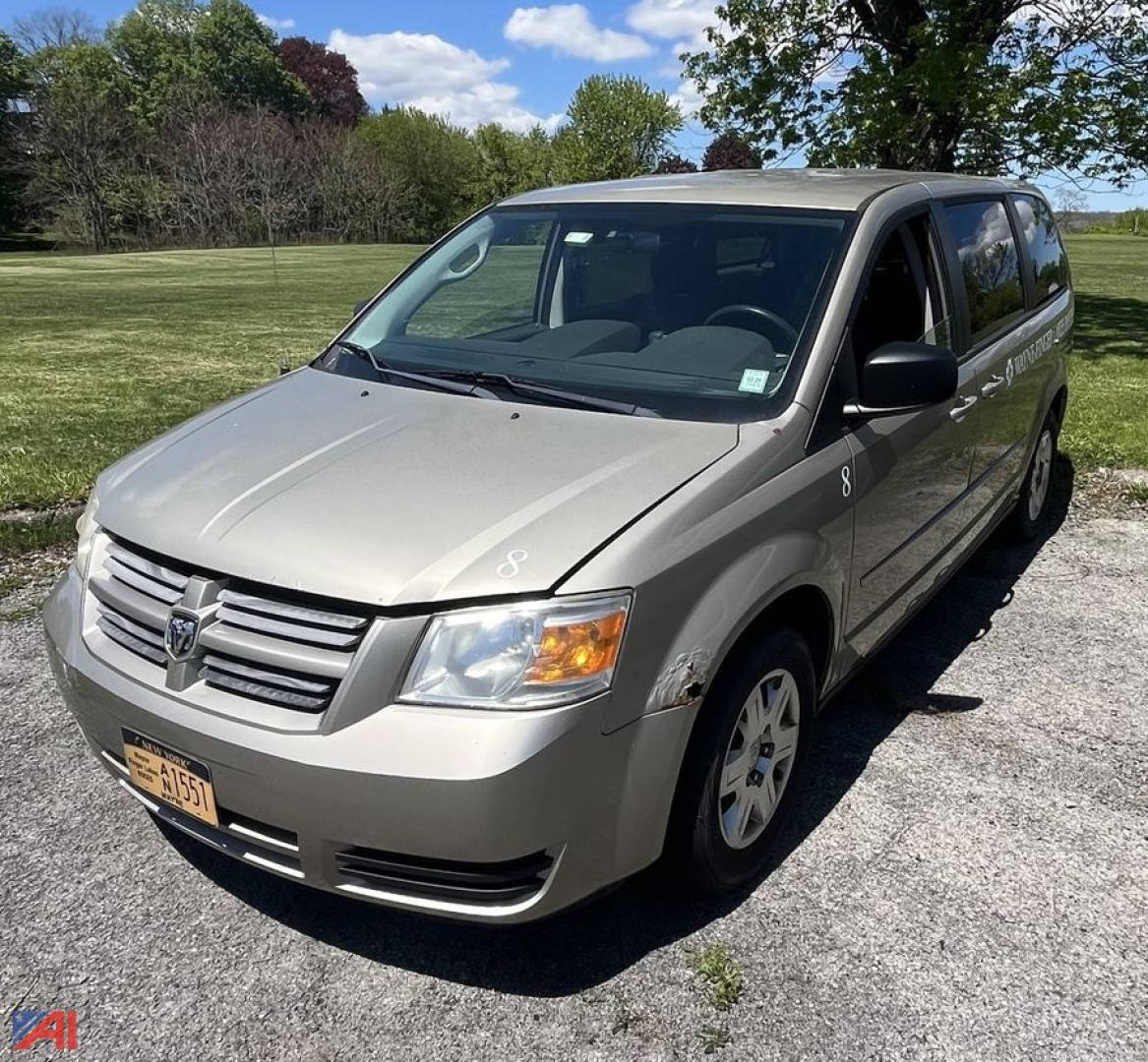 Dodge Grand Caravan minivan angled view showing front and passenger side, silver exterior, NY license plate, van style with sliding doors.