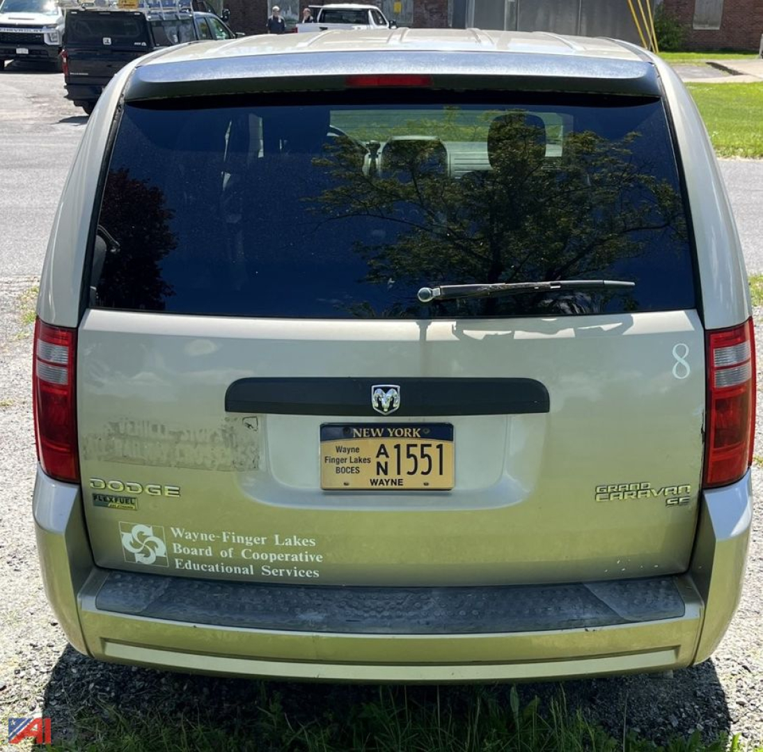 Rear view of a light-colored Dodge minivan showing tailgate with license plate and decals including Wayne-Finger Lakes BOE Educational Services.