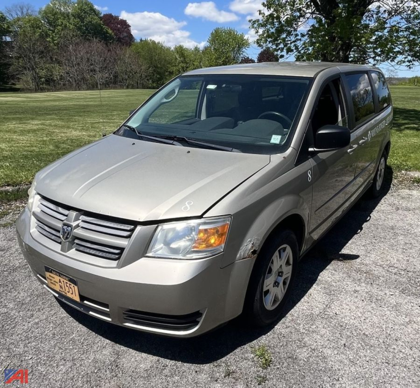 Dodge Grand Caravan minivan angled view showing front and passenger side, silver exterior, NY license plate, van style with sliding doors.