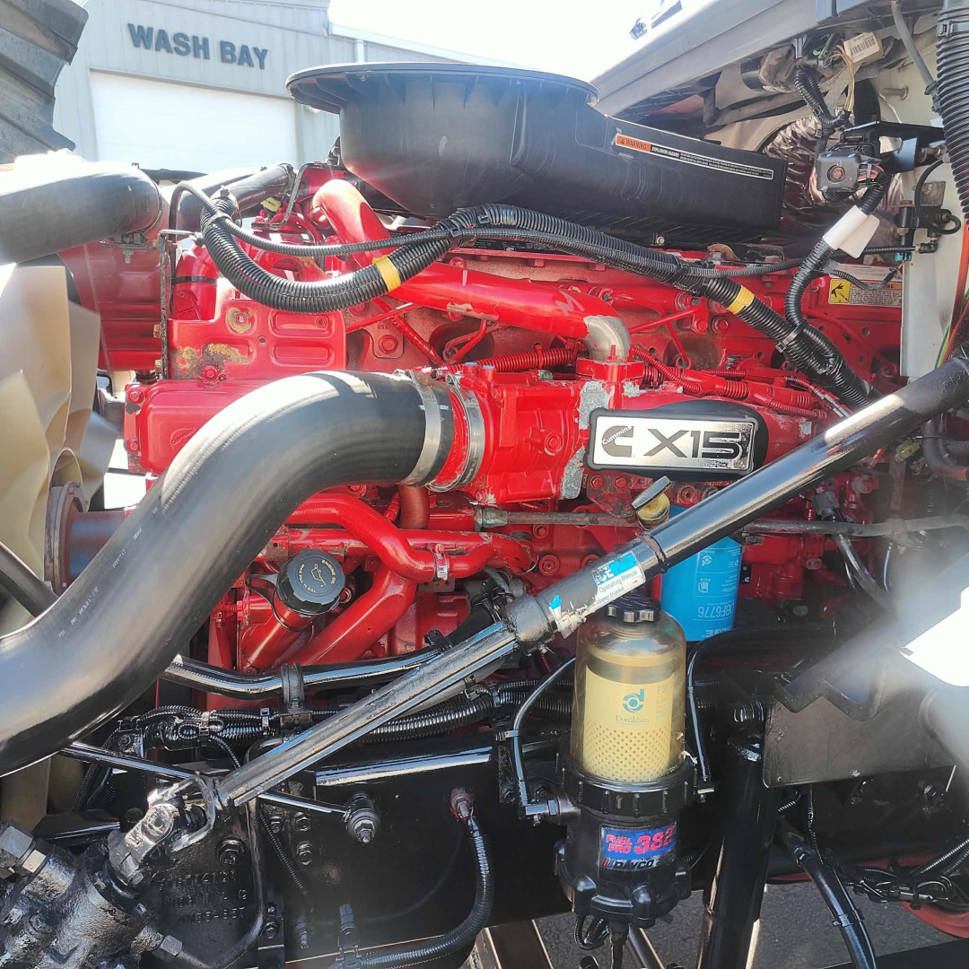 Engine bay of a red International LT truck showing Cummins CX15 badge, various hoses, filters, and components in the engine compartment.