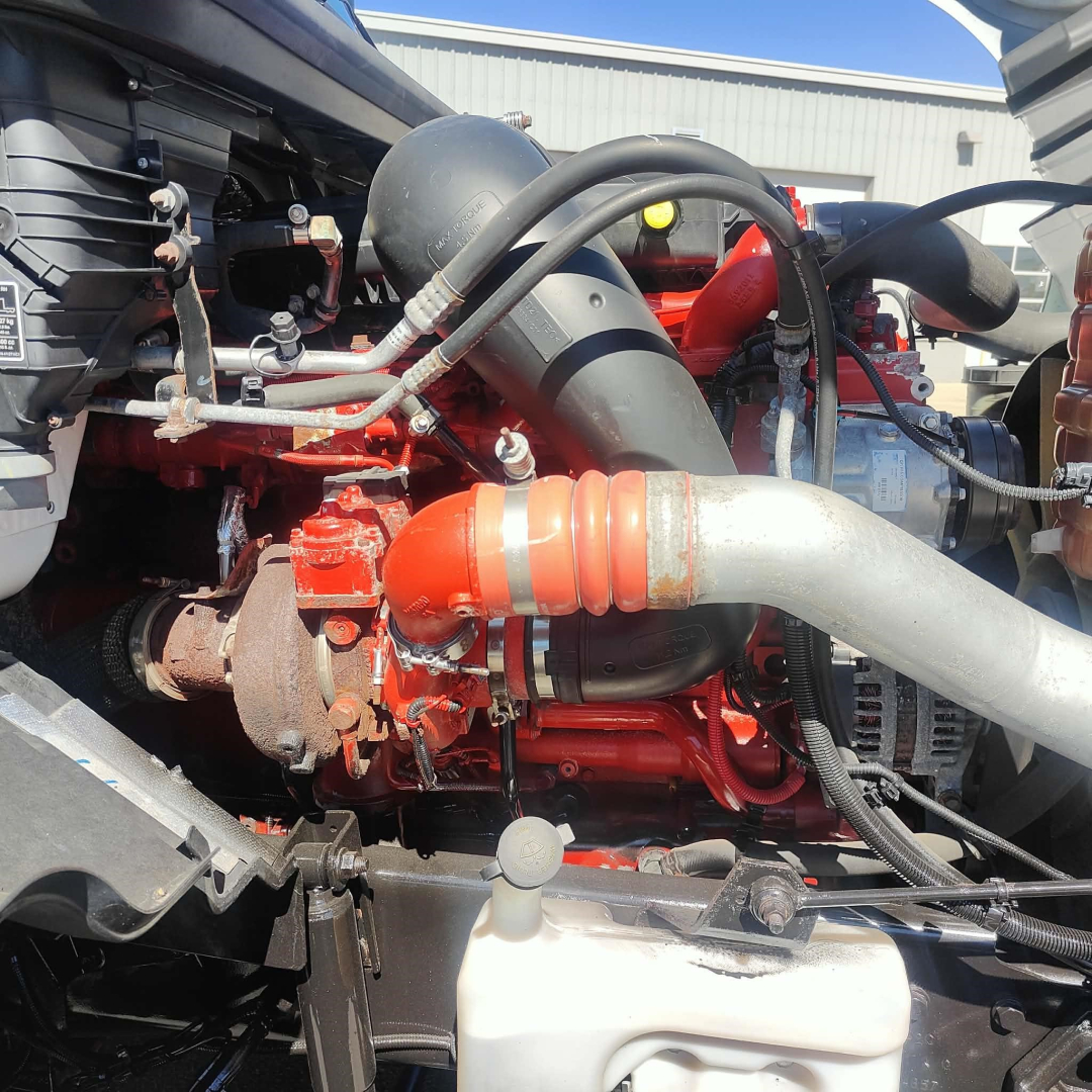 Engine bay showing red engine, orange silicone hose, large aluminum intake, black coolant reservoir hose, white plastic coolant reservoir, and various metal brackets.