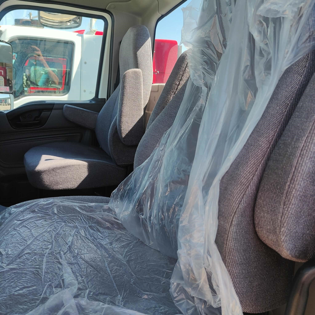 Interior of a 2021 International LT truck cab with fabric seats partially covered in plastic, view through window showing exterior units.