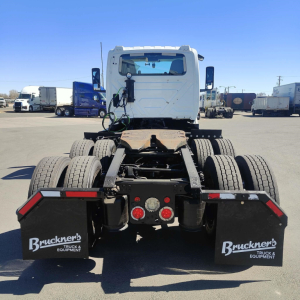 Truck chassis rear view showing dual rear axles, black mud flaps with Bruckner's Truck & Equipment logo, tail lights, and fifth-wheel area of a 2021 International LT conventional daycab.