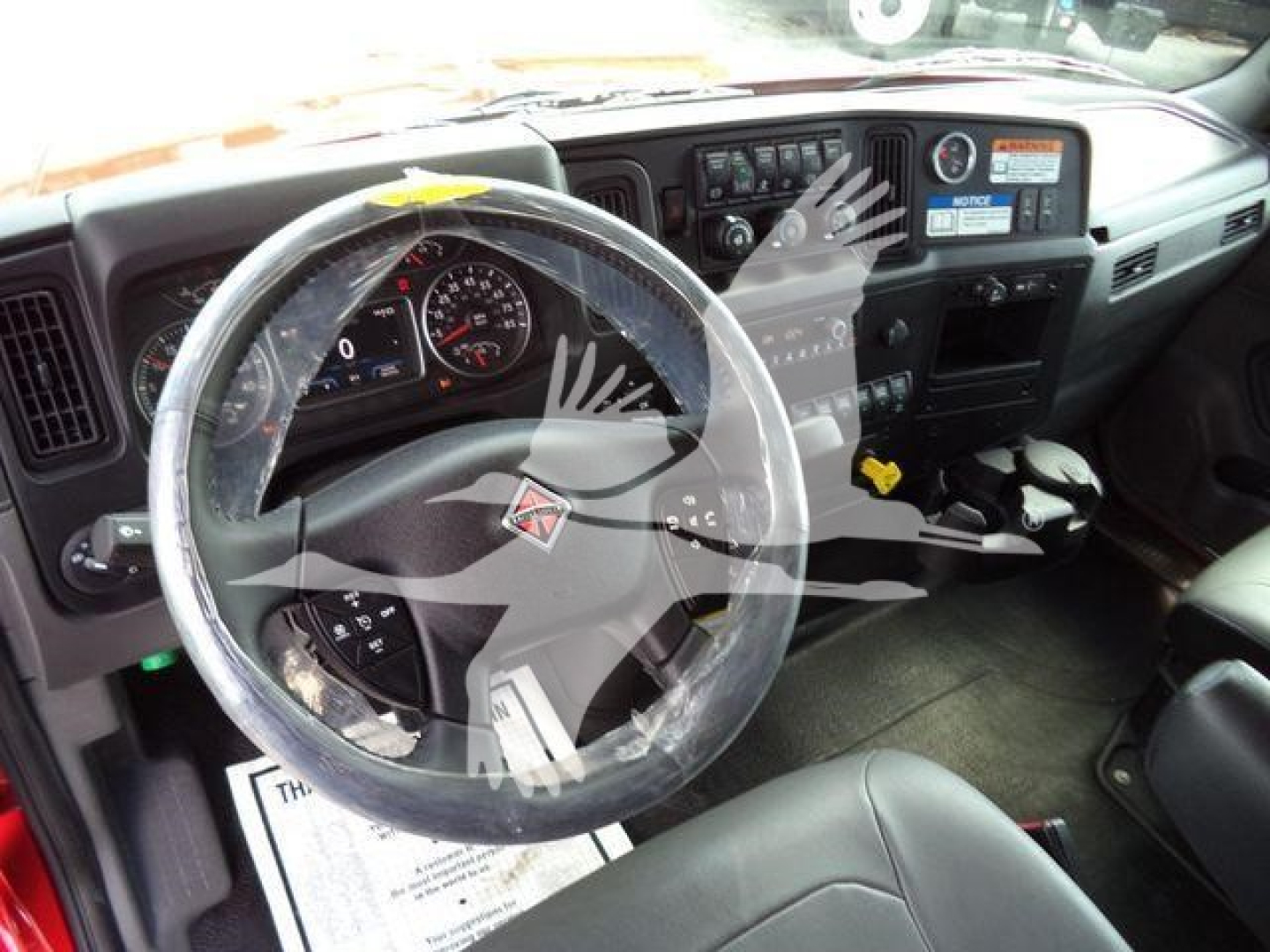 Truck cabin interior of a 2027 International MV showing steering wheel, instrument cluster, and dashboard controls.