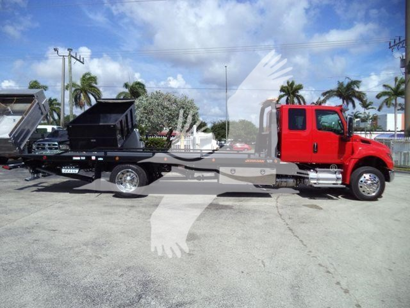 Flatbed rollback tow truck with red cab and blackbed, side view showing loading bed and hydraulic components.