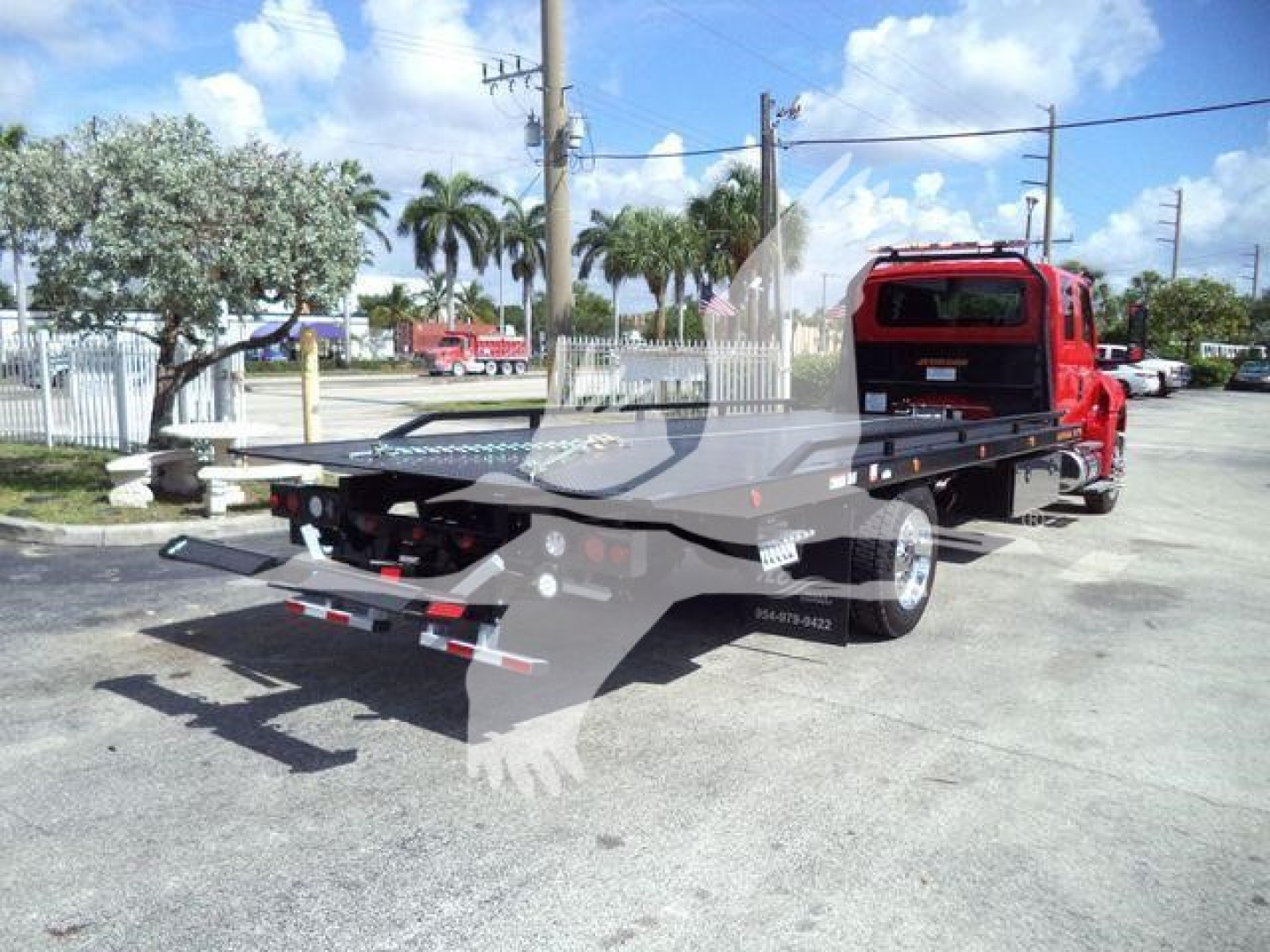 Tow truck with flatbed rollback in red cab showing rear flatbed and towing setup.