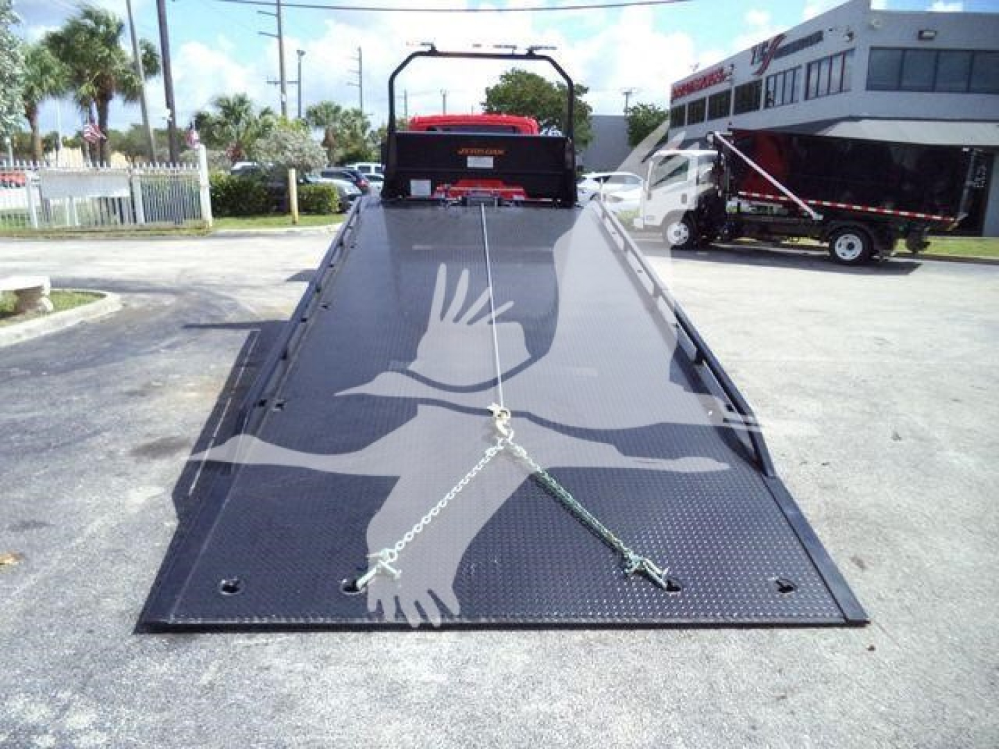 Flatbed tow truck bed with a large white eagle graphic, chains secured across the surface, and wheel ramps at the rear.